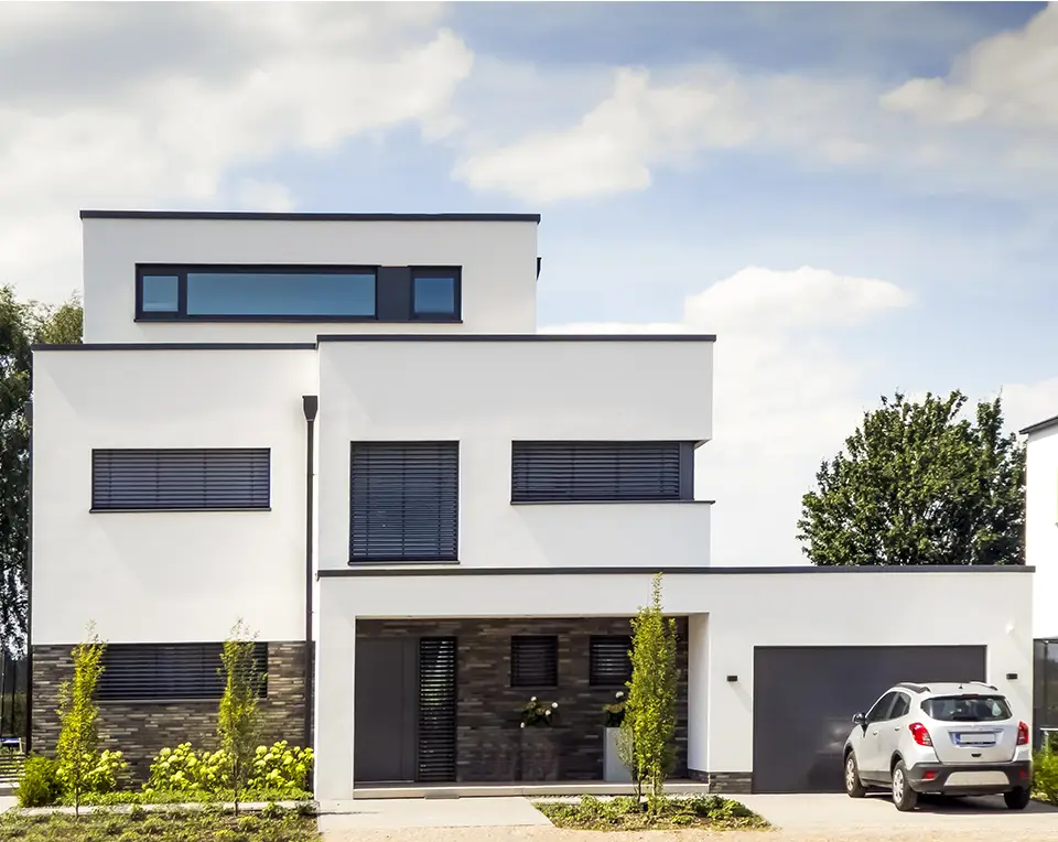 sundex-venkovni-hlinikove-zaluzie-rodinny-dum-313 Usměvavá žena stojí ve dveřích moderního obývacího pokoje a na mobilu právě ovládá venkovní hliníkové žaluzie na širokých oknech.
